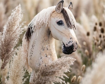 May include: A hobby horse with a cream-colored fabric head, featuring dark brown yarn mane and forelock details. The horse head has painted black eyes, a dark muzzle, and speckled markings on the neck, mounted on a wooden stick handle.