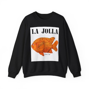 May include: Black sweatshirt featuring a large orange goldfish illustration within a white rectangle. The text "LA JOLLA" is above the fish, and the artist's signature is below. The sweatshirt is a casual garment.