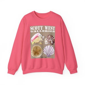 May include: A coral-colored sweatshirt featuring a graphic of various seashells and the text "SCOTT WEST GALLERIES." The design includes a conch shell, nautilus, sand dollar, and scallop shell. The sweatshirt is a crew neck style.