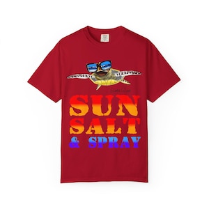 Pode incluir: Camiseta vermelha com uma tartaruga de desenho animado usando óculos de sol. O texto "SUN SALT & SPRAY" é impresso em um gradiente de laranja, amarelo, azul e roxo. O desenho da tartaruga está acima do texto.