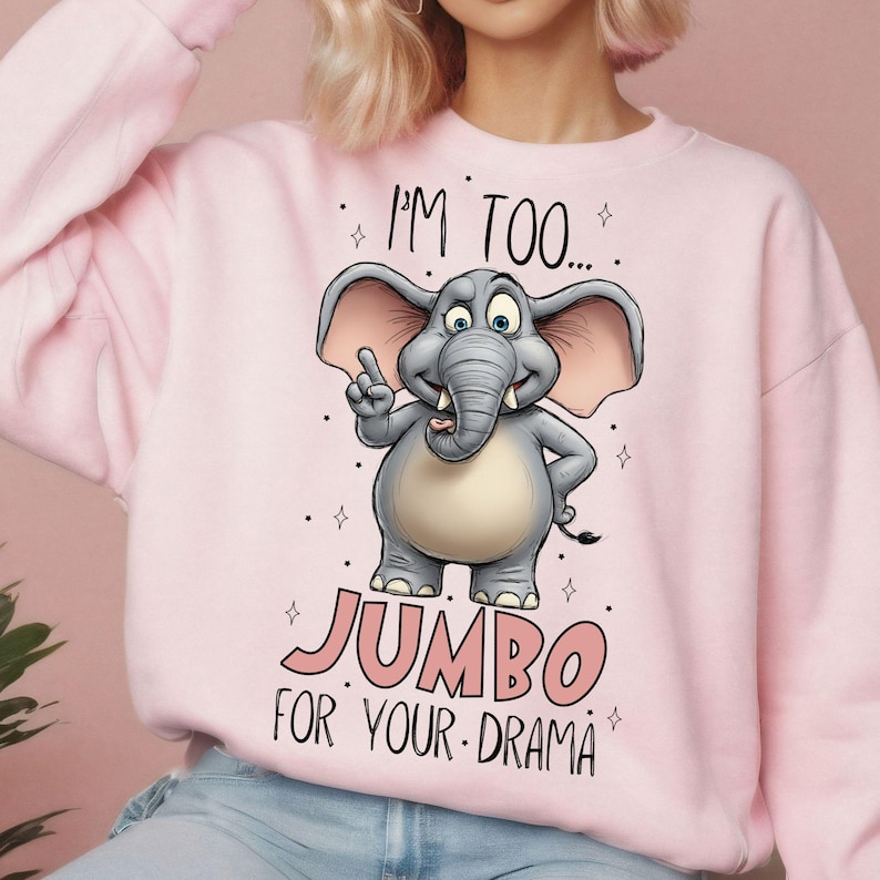May include: Pink sweatshirt featuring a cartoon elephant with the text "I'M TOO... JUMBO FOR YOUR DRAMA". The elephant is gray with pink ears and is pointing upwards. The text is in pink and the design is surrounded by small stars.