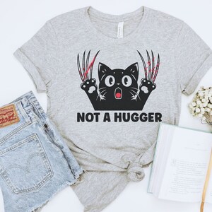 May include: Gray t-shirt with a black cat with red claws and the text "NOT A HUGGER".