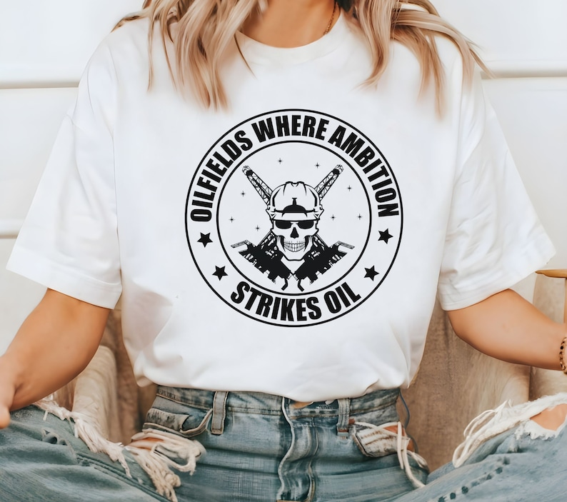 May include: White t-shirt with a black and white graphic of a skull wearing a hard hat and crossed oil derricks. The graphic is inside a circle with the text "Oilfields Where Ambition Strikes Oil".