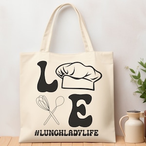 May include: A white canvas tote bag with black text and graphics. The text reads "LOVE" with a chef's hat between the "O" and "V".  There are two crossed whisks below the text. The text at the bottom reads "#LUNCHLADYLIFE".