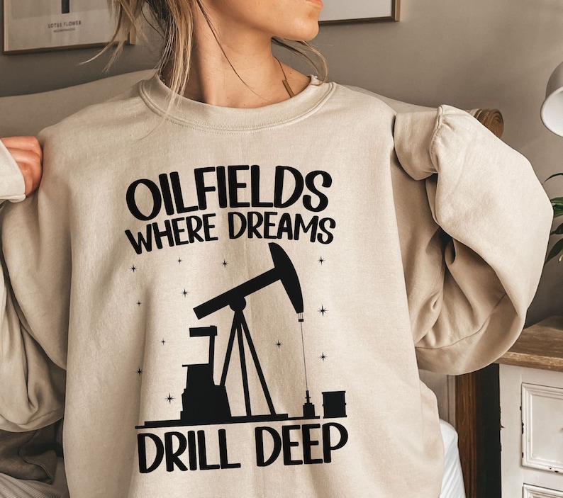 May include: A beige sweatshirt with a black graphic print of an oil rig and the text "Oilfields Where Dreams Drill Deep".