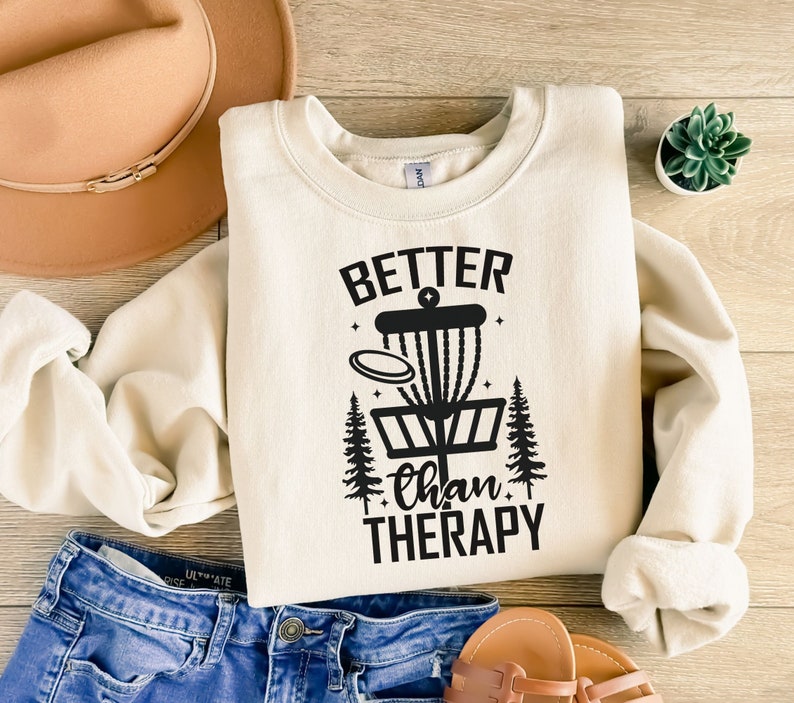 May include: A cream-colored sweatshirt with a black graphic of a disc golf basket and the text "Better than Therapy".