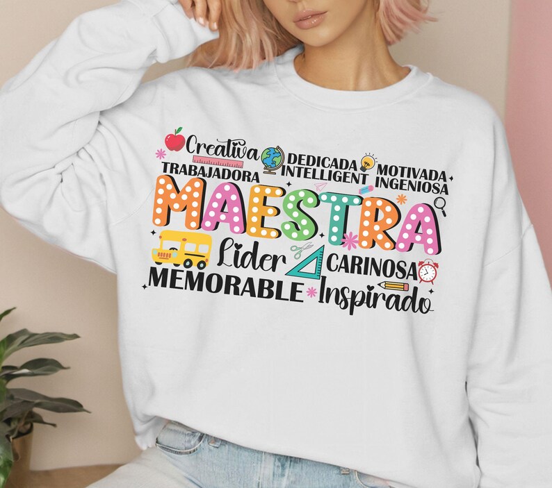 Pode incluir: Camisola branca com um design gr&aacute;fico colorido que diz "Maestra" e inclui palavras como "creativa", "trabajadora", "dedicada", "inteligente", "motivada", "ingeniosa", "lider", "cari&ntilde;osa", "memorable" e "inspirado".