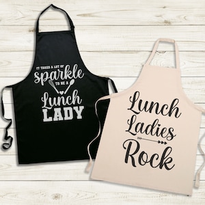 May include: Two black and white aprons with text. The black apron says "It takes a lot of sparkle to be a lunch lady". The white apron says "Lunch ladies rock".