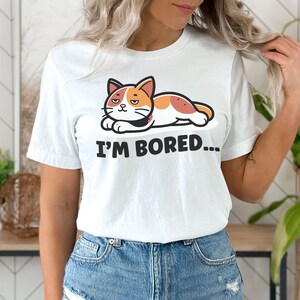 May include: White t-shirt with a cartoon cat lying down and the text "I'm Bored..." printed on it.