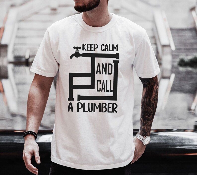 May include: White t-shirt with a black graphic that says "Keep Calm and Call a Plumber". The graphic features a stylized faucet and pipes.