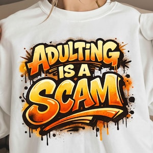 Pu&ograve; includere: Felpa bianca con la scritta "ADULTING IS A SCAM" in grandi lettere arancioni e gialle in stile graffiti. Il design include gocce e schizzi neri, creando un'affermazione audace e accattivante.