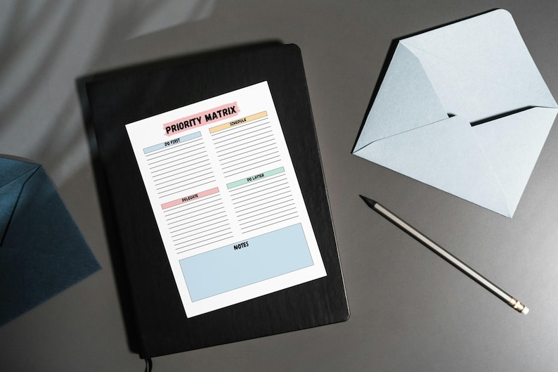 May include: A black notebook with a white sheet of paper on top. The paper has a priority matrix with the words "Do First", "Delegate", "Do Later", and "Don't Do" in colored boxes. The paper also has a section for notes.