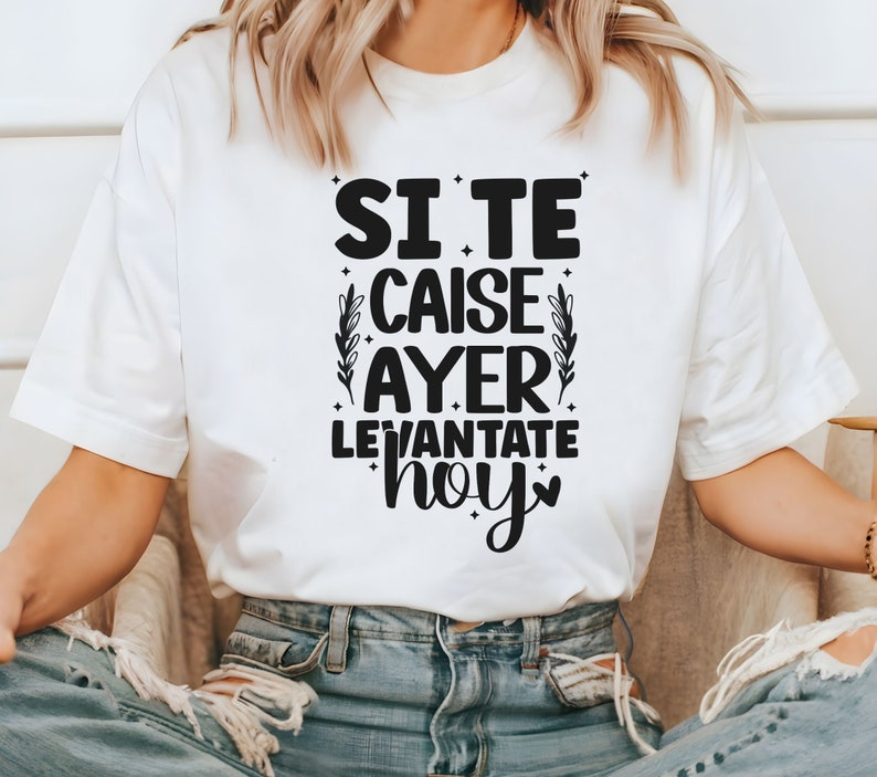 May include: White t-shirt with black text that reads "Si te caise ayer levantate hoy" with a small heart symbol. The text is surrounded by small black stars and a floral design.