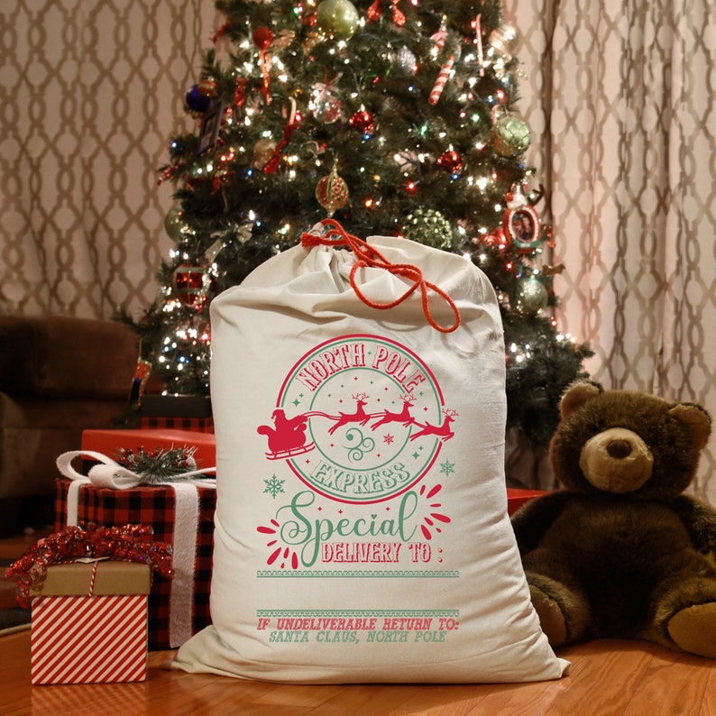 May include: A white canvas Santa sack with a red drawstring. The sack has a red and green graphic of Santa Claus in his sleigh with reindeer, a North Pole Express stamp, and the text "Special Delivery To:".