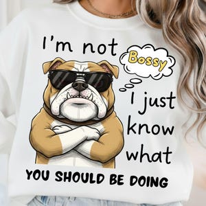 May include: White sweatshirt featuring a cartoon bulldog wearing sunglasses with arms crossed. The text reads "I'm not bossy, I just know what you should be doing."