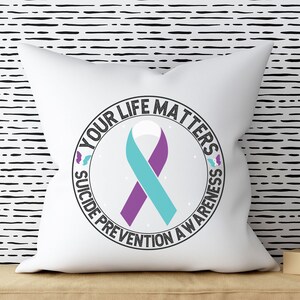 以下が含まれることがあります： 中央にターコイズブルーとパープルのリボンがついた、"Your Life Matters Suicide Prevention Awareness"と書かれた黒い円形のデザインが施された白い枕
