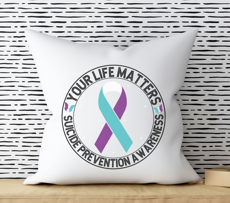 以下が含まれることがあります： 中央にターコイズブルーとパープルのリボンがついた、"Your Life Matters Suicide Prevention Awareness"と書かれた黒い円形のデザインが施された白い枕