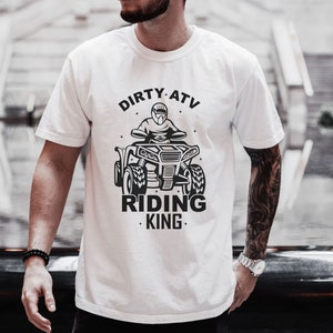 May include: White t-shirt with a black graphic of a person riding an ATV. The text "DIRTY ATV RIDING KING" is printed on the shirt.