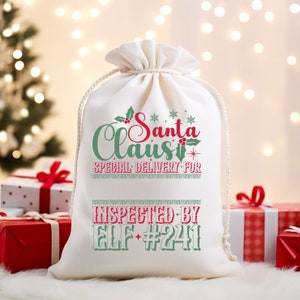 May include: White canvas gift bag with red and green text that reads "Santa Claus Special Delivery For" and "Inspected By Elf #241".