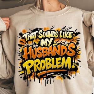 Pu&ograve; includere: Felpa beige con la scritta "THAT SOUNDS LIKE MY HUSBAND'S PROBLEM!" in un design in stile graffiti. Il testo &egrave; giallo e arancione, con dettagli neri e floreali.