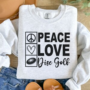 May include: A gray sweatshirt with the text "Peace Love Disc Golf" in black. The text is surrounded by three icons: a peace sign, a heart, and a disc golf disc.