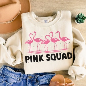 Puede incluir: Una sudadera de color crema con un gr&aacute;fico de flamencos rosas y el texto "PINK SQUAD".
