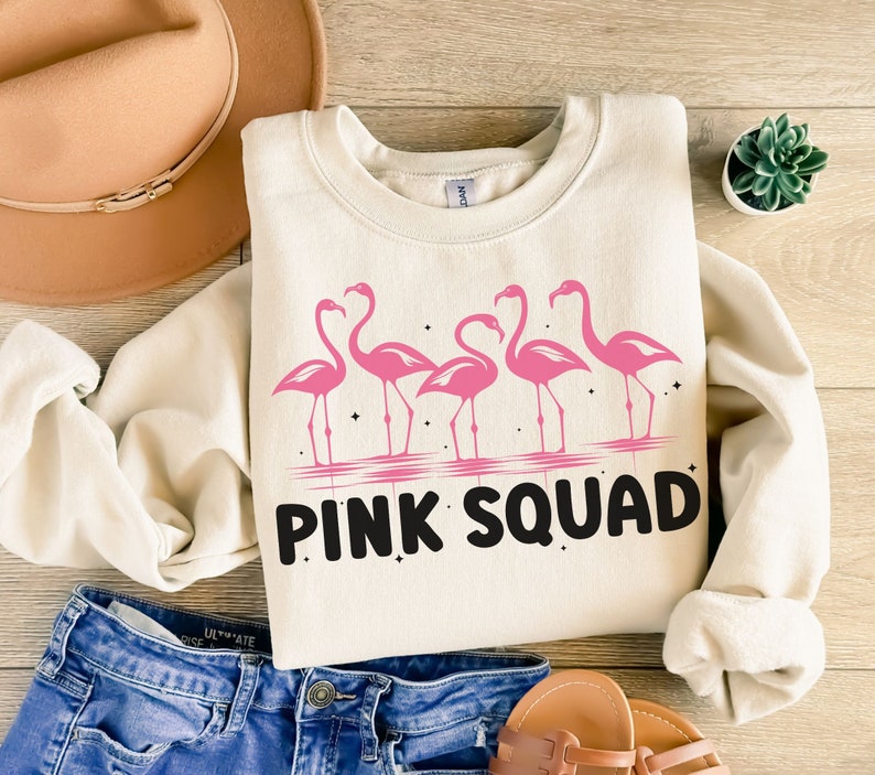 Puede incluir: Una sudadera de color crema con un gr&aacute;fico de flamencos rosas y el texto "PINK SQUAD".