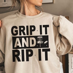 May include: A beige sweatshirt with black text that reads "Grip It And Rip It" with a disc golf disc graphic.