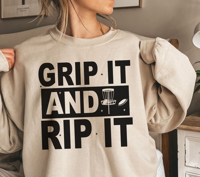 May include: A beige sweatshirt with black text that reads "Grip It And Rip It" with a disc golf disc graphic.