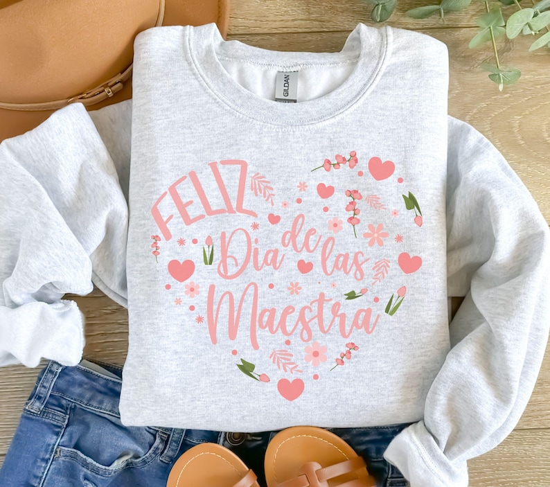 Pode incluir: Camisola cinzenta com um desenho de cora&ccedil;&atilde;o rosa que diz "Feliz Dia de las Maestra" em letras cor-de-rosa.