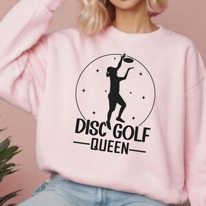 May include: Pink sweatshirt with a black graphic of a person throwing a disc, a circle with stars, and the text "Disc Golf -Queen-"