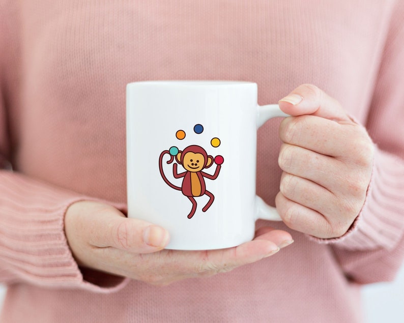 May include: White ceramic mug with a cartoon monkey juggling colorful balls. The monkey is brown with a yellow belly and has a red nose. The balls are red, yellow, blue, and green.