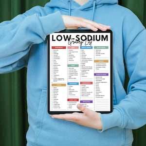 May include: A person holding a digital tablet displaying a low-sodium grocery list. The list is organized by food category and includes a checkbox next to each item.