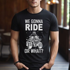 May include: Black t-shirt with a white graphic of a person riding an ATV. The text on the shirt reads "We gonna ride or what?"