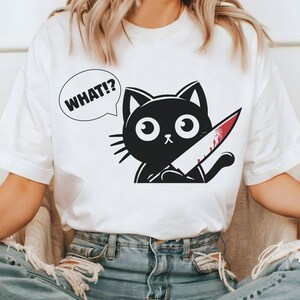 May include: White t-shirt with a black cat holding a bloody knife and a speech bubble that says "WHAT!?"
