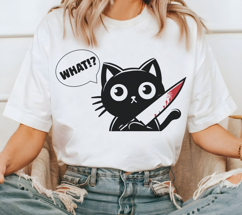 May include: White t-shirt with a black cat holding a bloody knife and a speech bubble that says "WHAT!?"