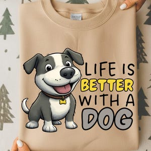 May include: Tan sweatshirt featuring a cartoon dog with a brown collar and a tag. The text "LIFE IS BETTER WITH A DOG" is printed in yellow and gray. The sweatshirt is a neutral color.