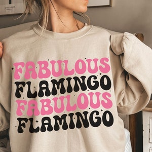 Puede incluir: Una sudadera beige con el texto "Fabulous Flamingo Fabulous Flamingo" en letras rosas y negras.