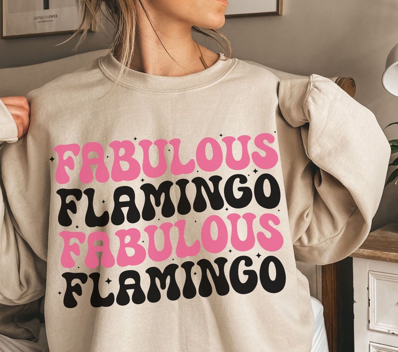 Puede incluir: Una sudadera beige con el texto "Fabulous Flamingo Fabulous Flamingo" en letras rosas y negras.