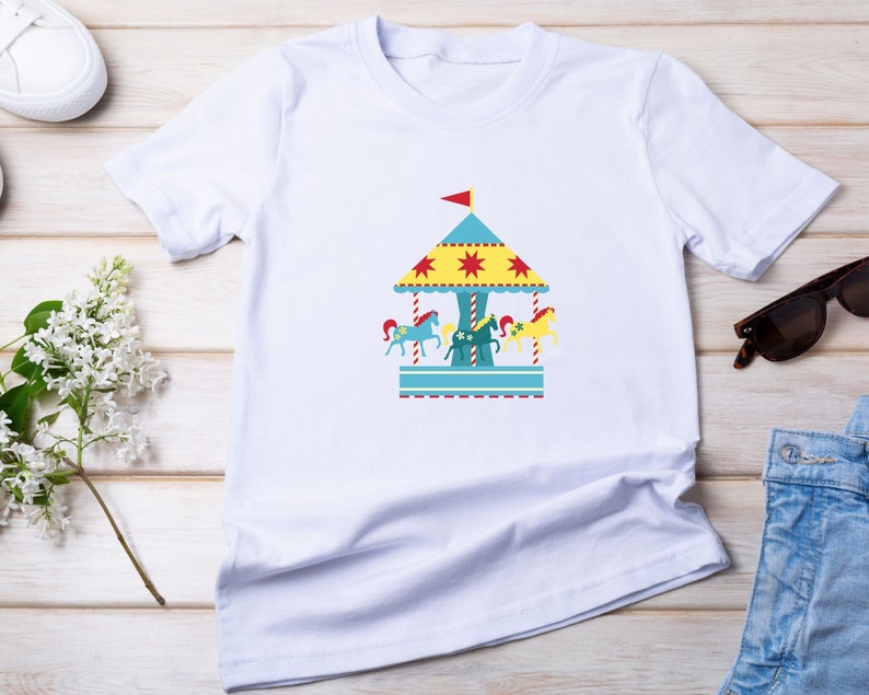 May include: White t-shirt with a colorful carousel design featuring a blue roof, yellow stars, and red and yellow horses.
