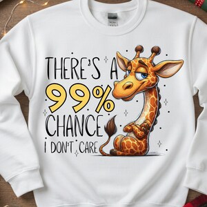May include: White sweatshirt featuring a cartoon giraffe with a smug expression. The giraffe has a brown and orange spotted pattern. Text on the sweatshirt reads "THERE'S A 99% CHANCE I DON'T CARE" in black and yellow.
