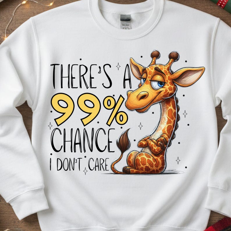 May include: White sweatshirt featuring a cartoon giraffe with a smug expression. The giraffe has a brown and orange spotted pattern. Text on the sweatshirt reads "THERE'S A 99% CHANCE I DON'T CARE" in black and yellow.