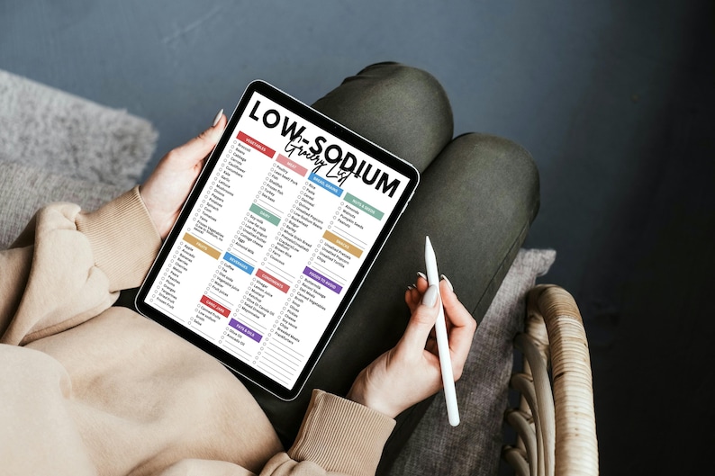May include: A digital tablet displaying a low sodium grocery list with checkboxes. The list is organized by category and includes a variety of food items. The tablet is being held by a person's hands.