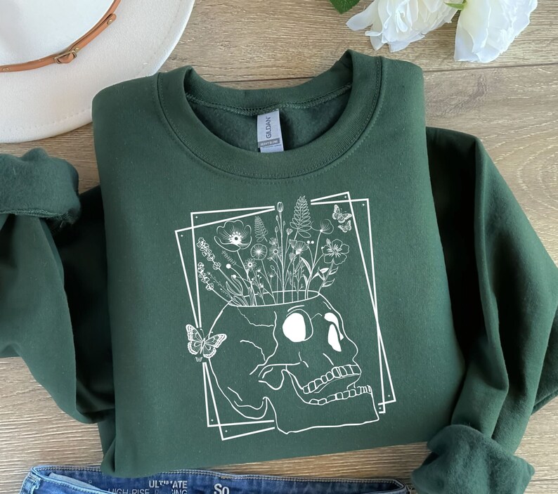 May include: A dark green sweatshirt with a white graphic of a skull with flowers growing out of the top. The skull is outlined in a white square.
