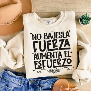 May include: A cream-colored sweatshirt with the text "No bajes la fuerza aumenta el esfuerzo" in black lettering.