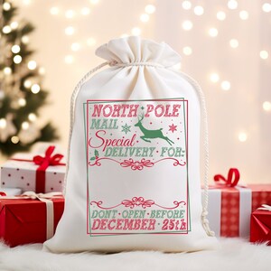 May include: White canvas gift bag with a red and green design. The bag has the text "North Pole Mail Special Delivery For:" and a reindeer illustration. The bottom of the bag says "Don't Open Before December 25th."