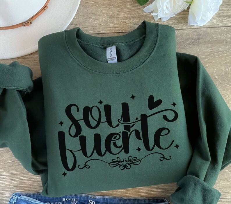 May include: A dark green sweatshirt with the text "soy fuerte" in black lettering. The text is in a stylized font with a heart and stars.