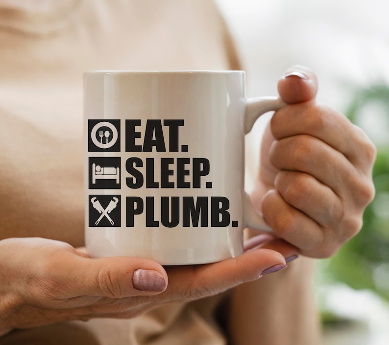 May include: White ceramic mug with black text that reads "Eat. Sleep. Plumb."  The mug has a black and white icon of a fork and spoon, a bed, and a wrench and pipe.