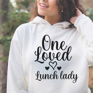 May include: White hoodie with black text that reads "One Loved Lunch Lady" with three small hearts.