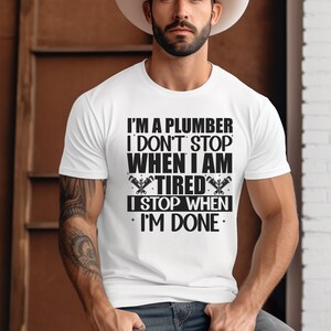 May include: White t-shirt with a black graphic that reads "I'm a plumber I don't stop when I am tired I stop when I'm done".